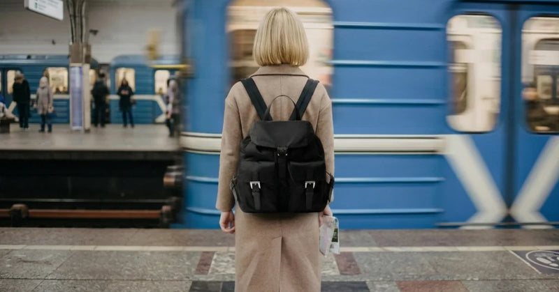 Woman wearing a black designer leather backpack on a subway platform as a train passes