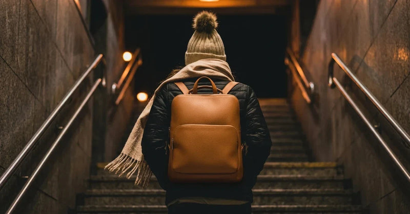 Woman carrying a tan leather backpack up the stairs of a subway station