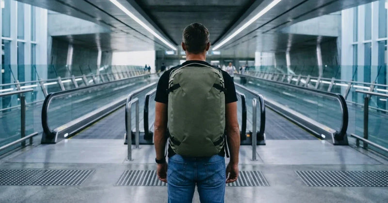 A man seen from behind carrying an olive travel backpack through an airport walkway