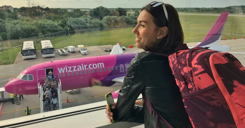 Traveller wearing a backpack watches passengers board a Wizz Air plane from an airport window