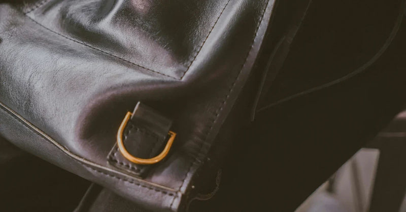 A dark glossy coated bag surface with a brass D-ring, the coating still intact