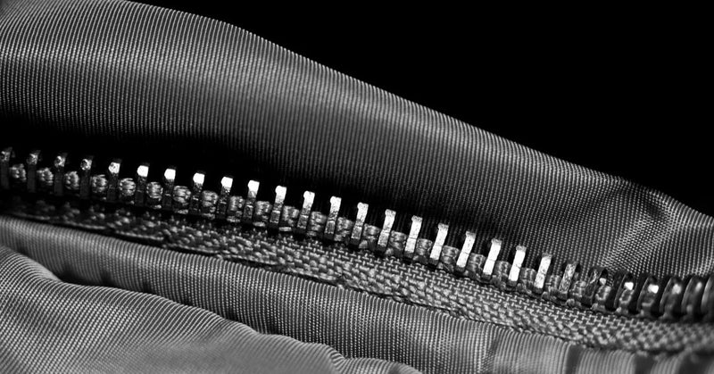 Close-up of a metal-toothed zipper lying half open on a nylon bag, lit hard against a black background