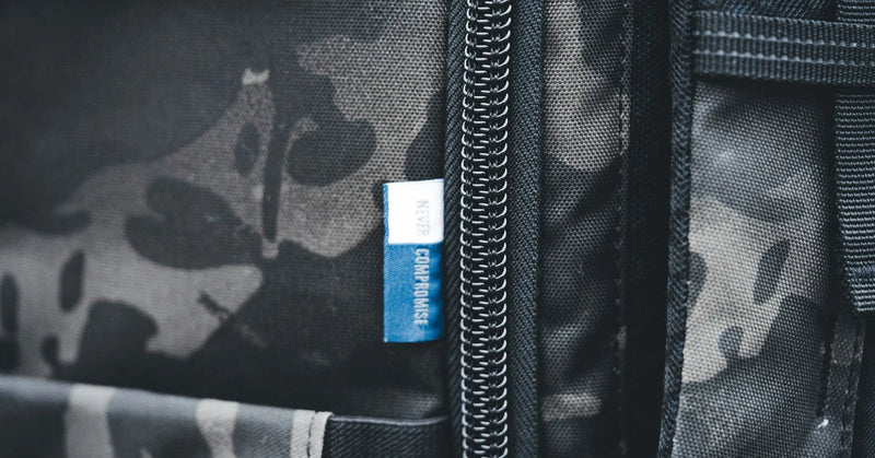 Macro close-up of a black camouflage backpack panel with a heavy metal zipper and woven fabric