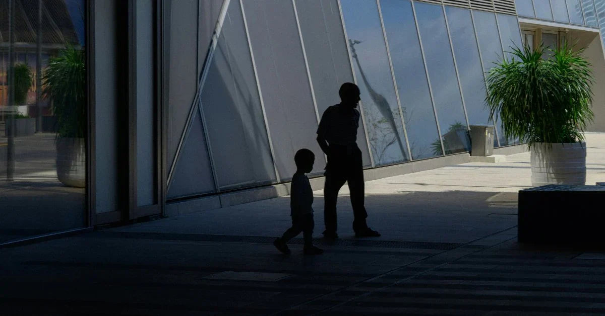 A parent and child walking through modern urban architecture, silhouetted against glass panels